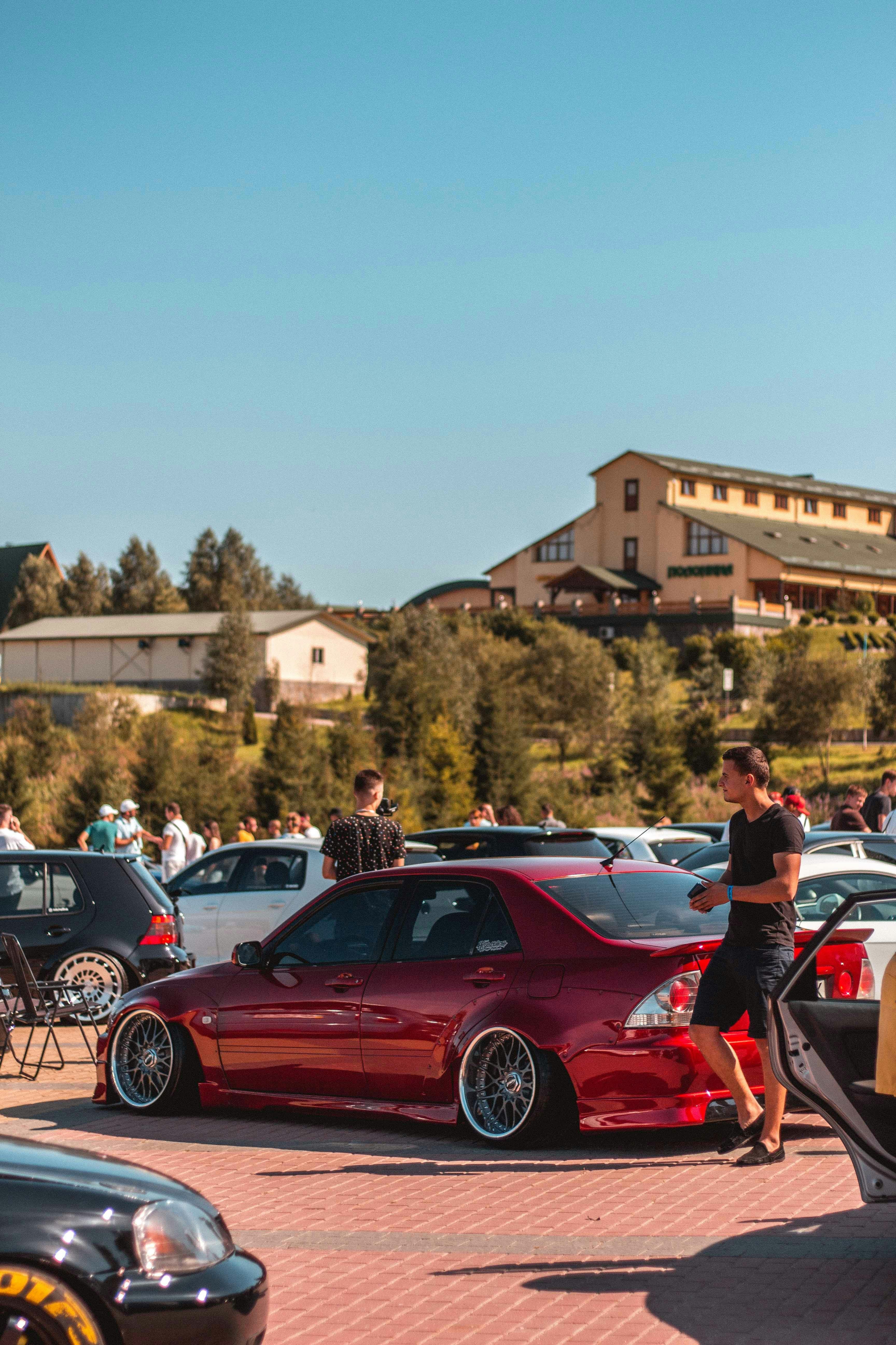 Red sports car parked at a car meet with enthusiasts gathering around it
