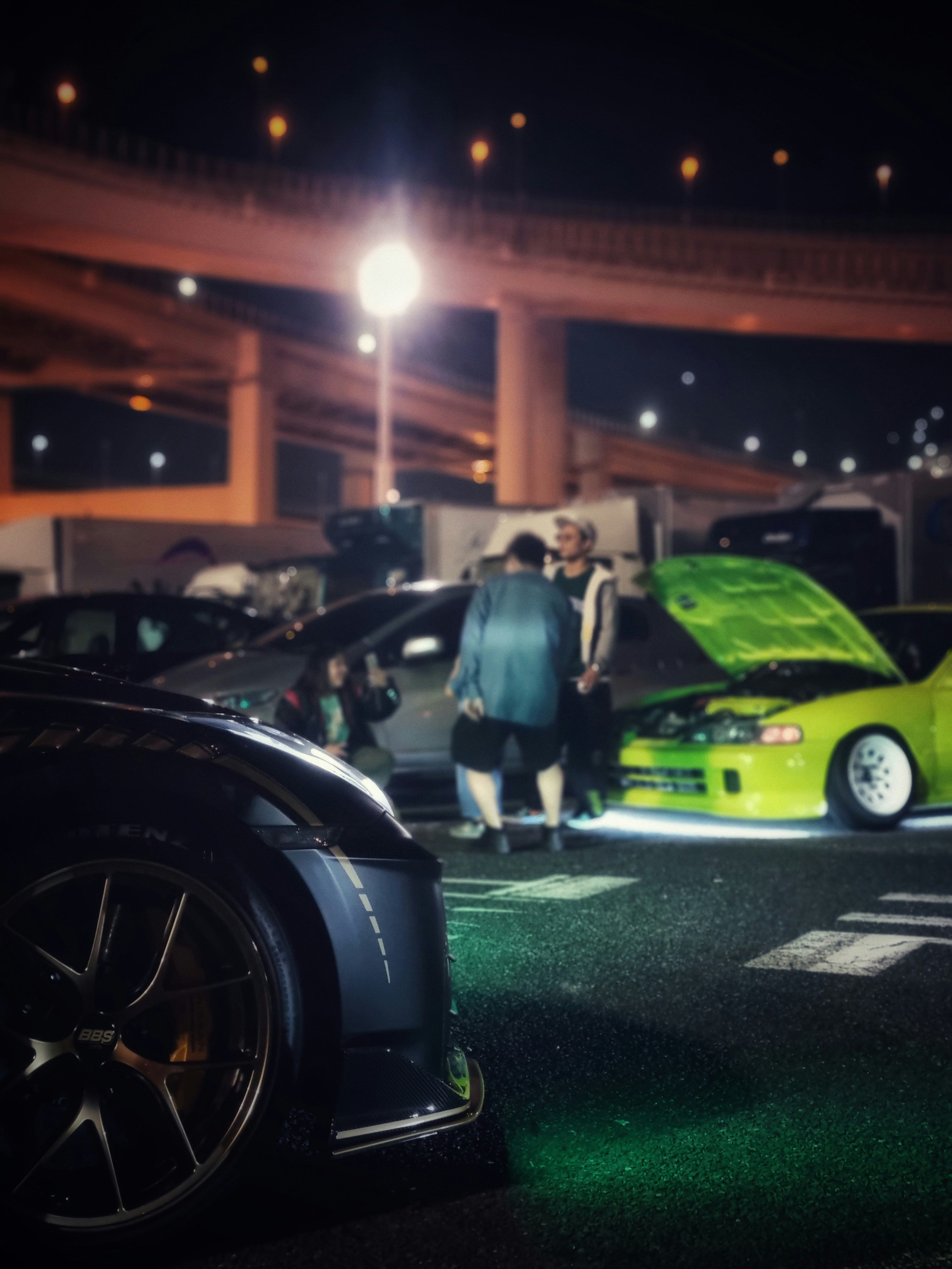 Dozens of modified cars lined up at a night meet in downtown St. Louis with city lights in background